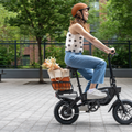 Woman riding an electric bike with a basket full of flowers on a sidewalk.