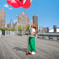 young kid holding onto balloons and a red jupiter kick scooter