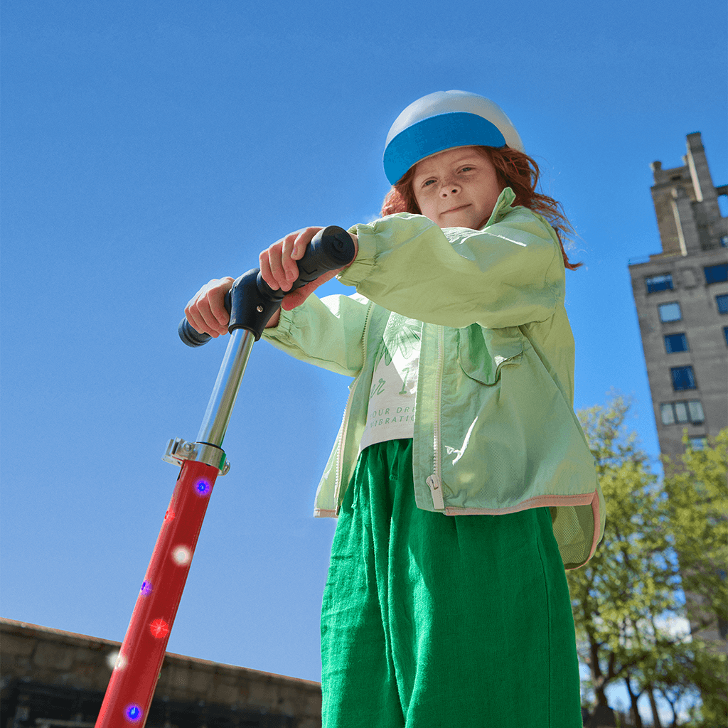 young kid holding onto handlebars of red jupiter kick scooter