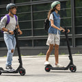 two young people riding the Rhythm e-scooter outside