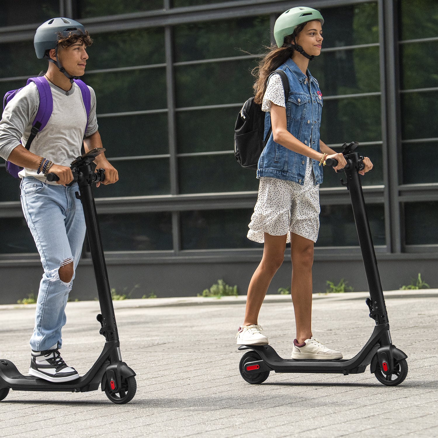 two young people riding the Rhythm e-scooter outside