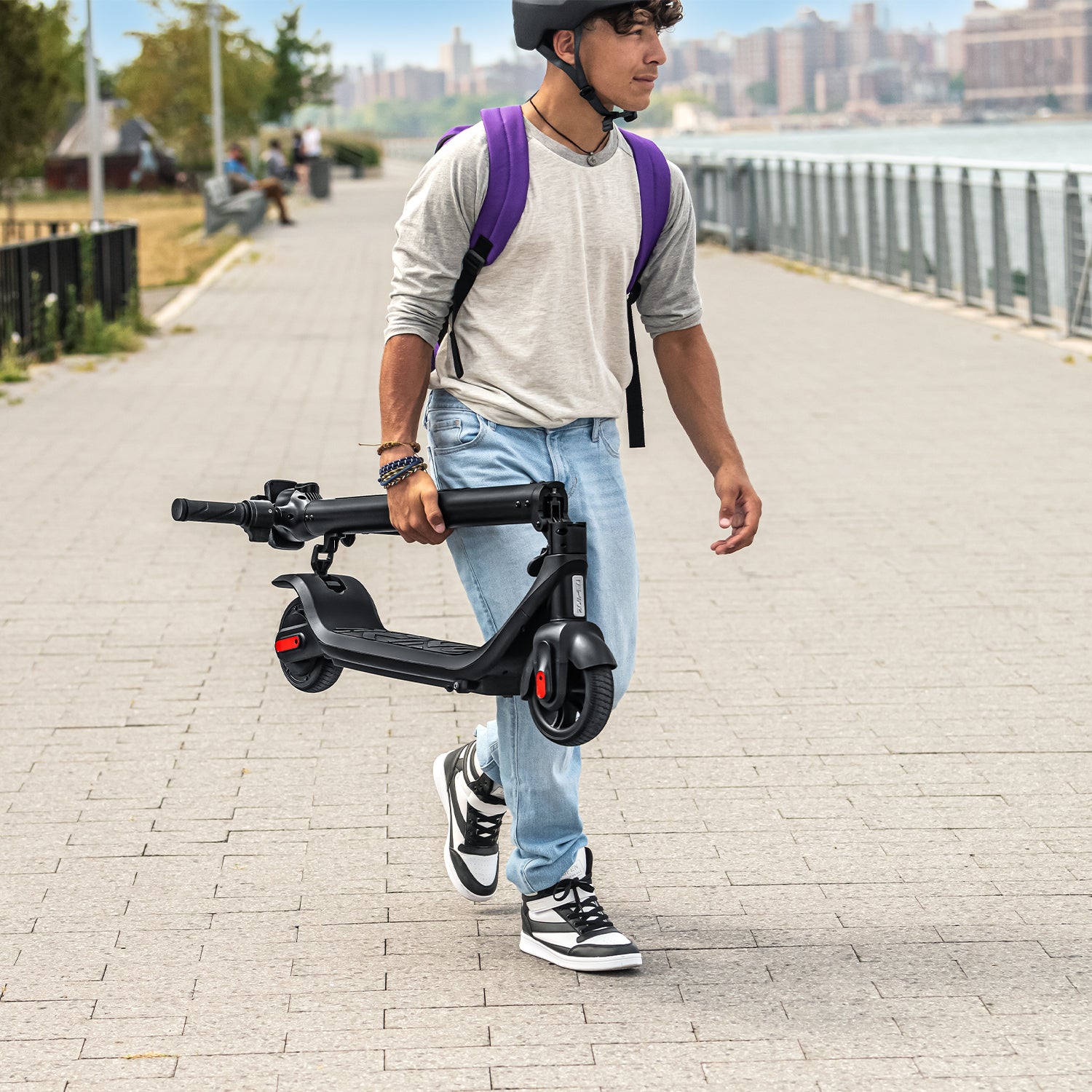 a young person carrying a folded Rhythm e-scooter