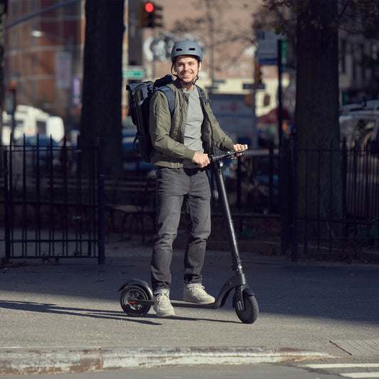 man standing with the knight scooter on the sidewalk