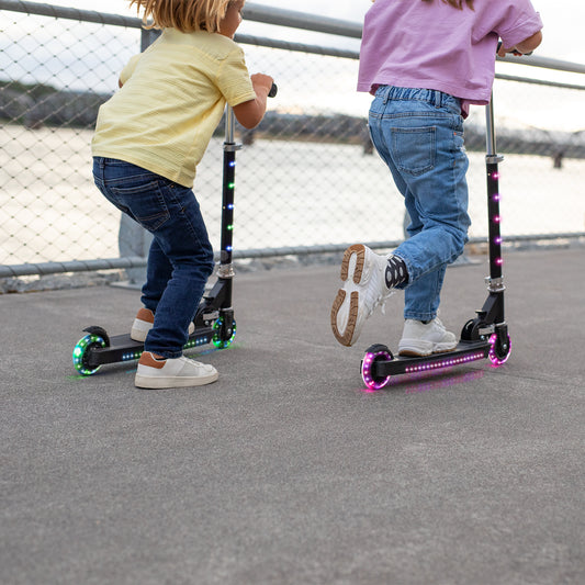two kids riding the light up orbit scooters along a paved path