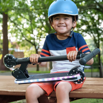kid seated with helmet on holding folded orbit x scooter