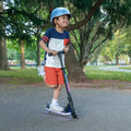 kid riding orbit x kick scooter through the park while wearing helmet