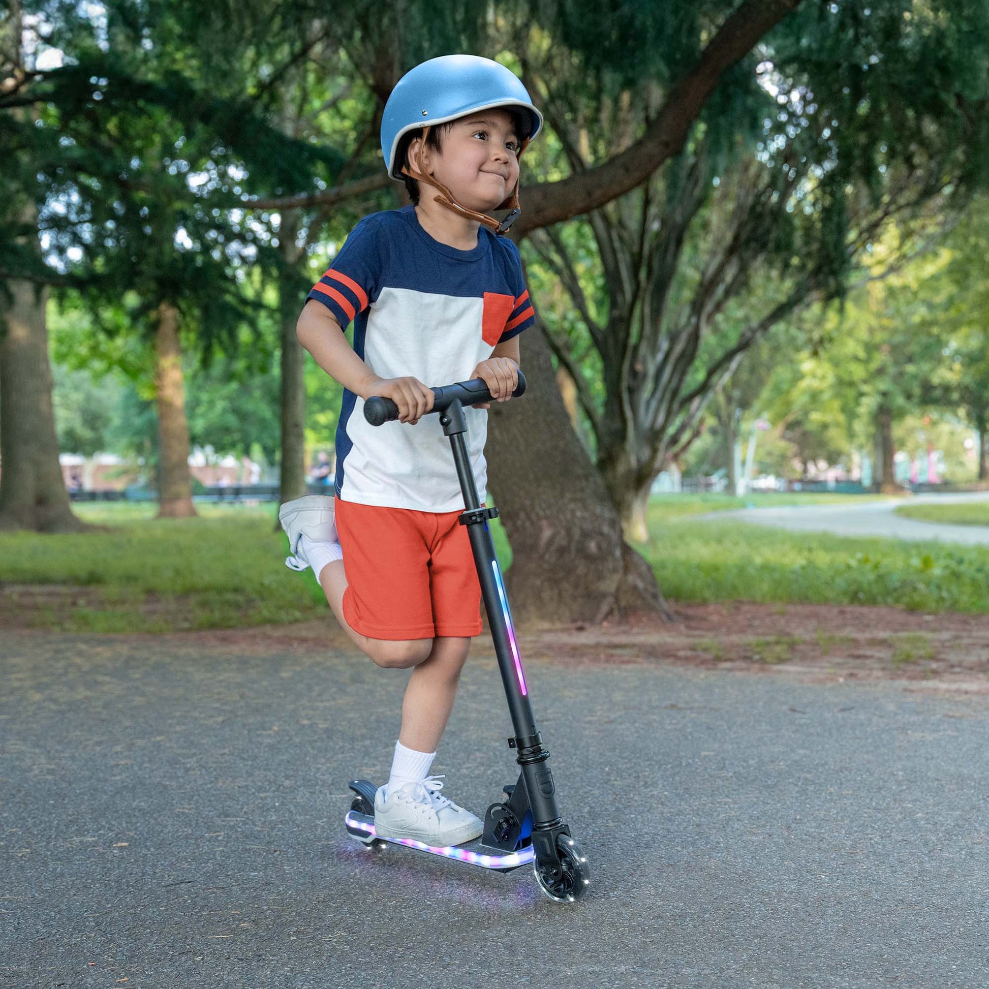 kid riding orbit x kick scooter through the park while wearing helmet