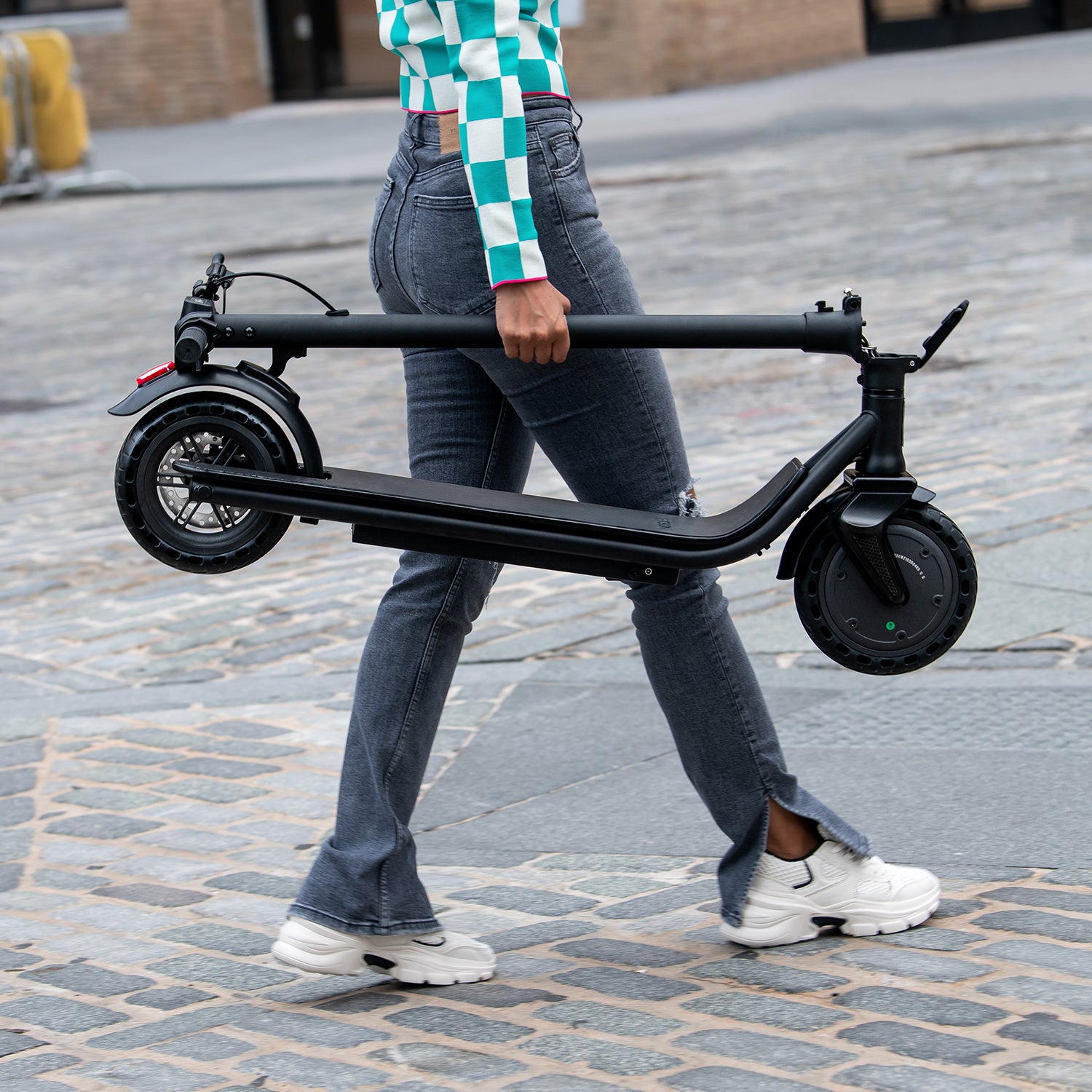 person carrying the folded racer scooter as they cross the street