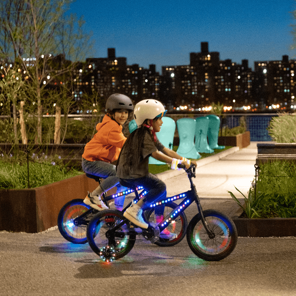 two kids riding black light up bikes on pavement