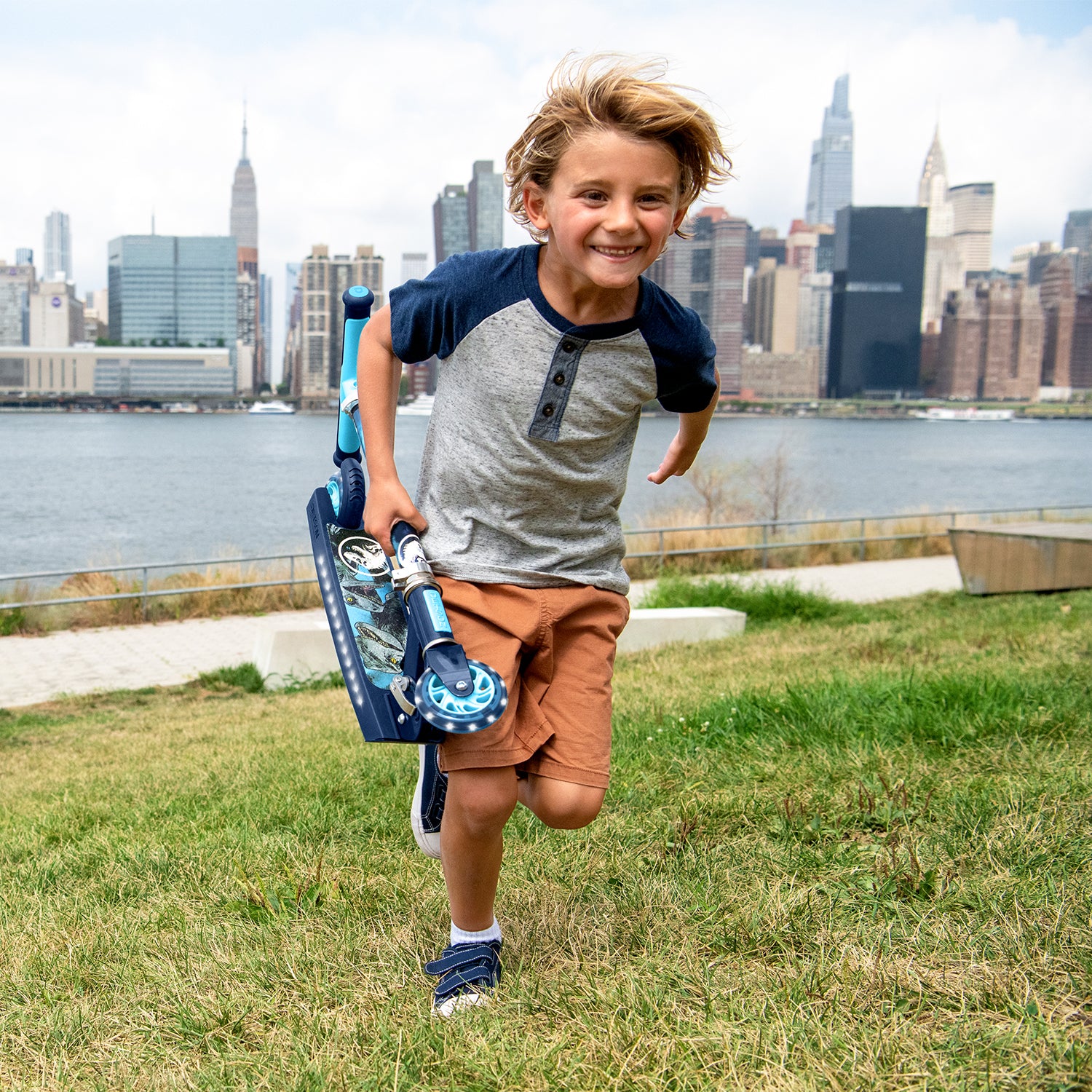 kid carrying a folded jurassic park kick scooter through the grass