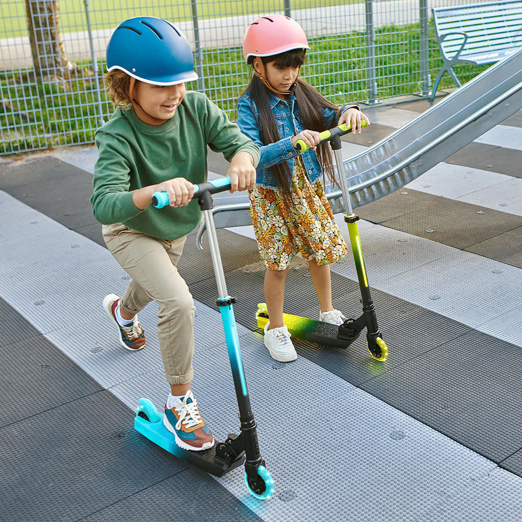 two kids riding blue and yellow juno kick scooters in a playground
