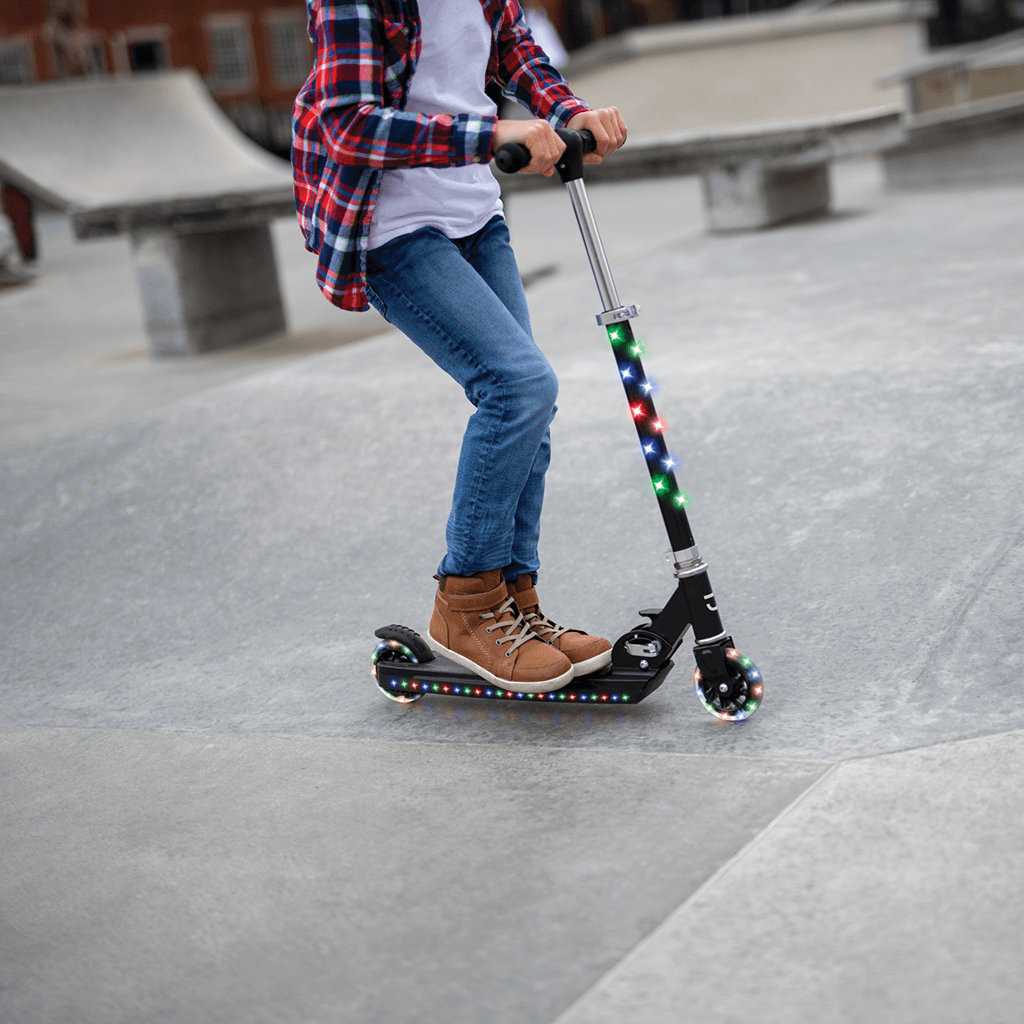young kid riding black jupiter kick scooter in a skate park