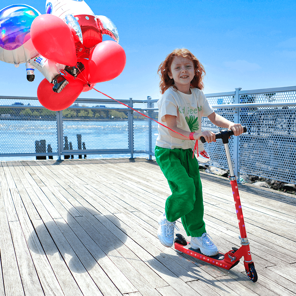 young kid riding red jupiter kick scooter on a boardwalk
