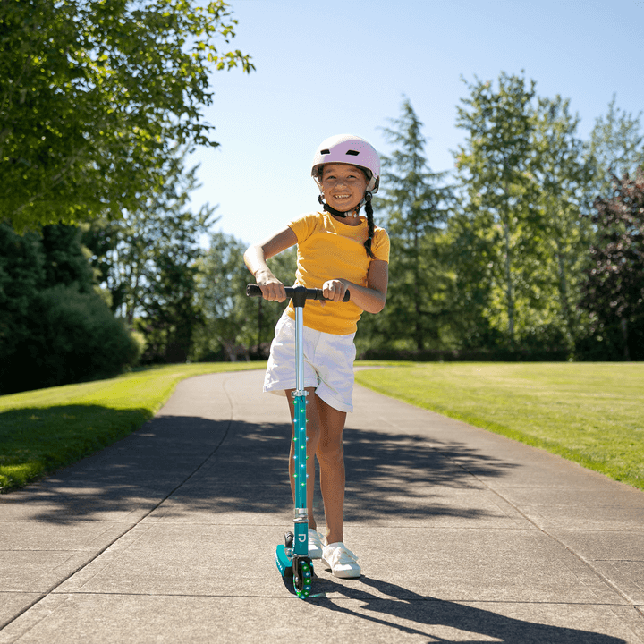 young kid riding a teal light up jupiter kick scooter in the park