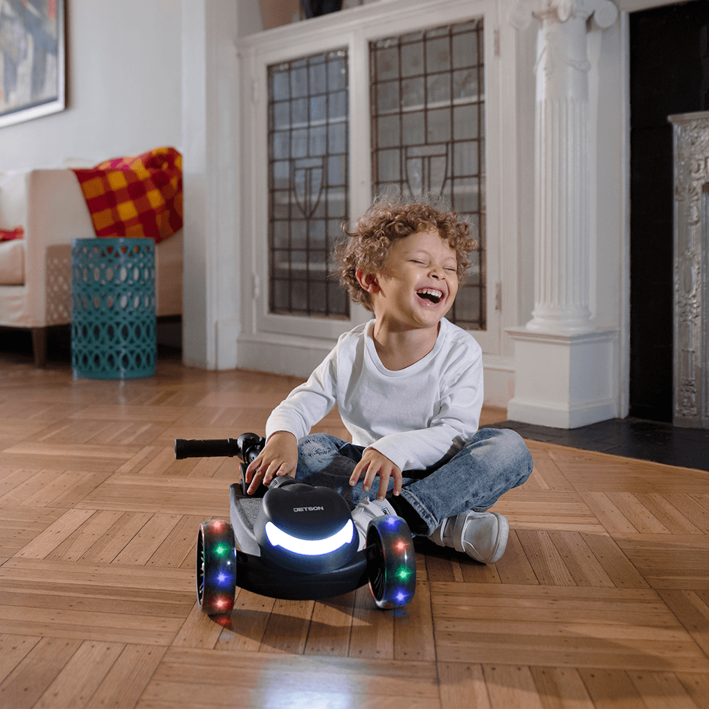 young kid sitting next to a folded jupiter mini kick scooter in the living room