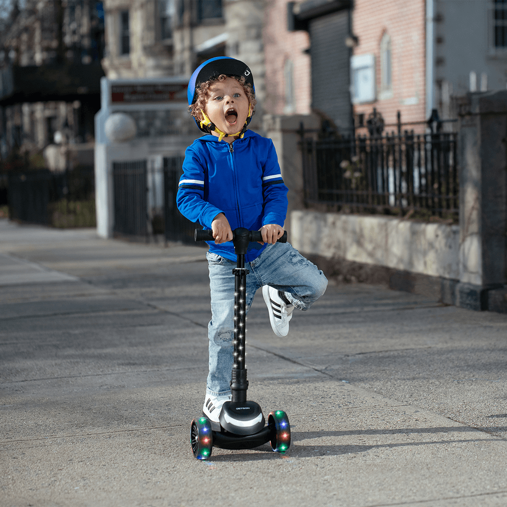young kid riding black jupiter mini kick scooter outside on the sidewalk