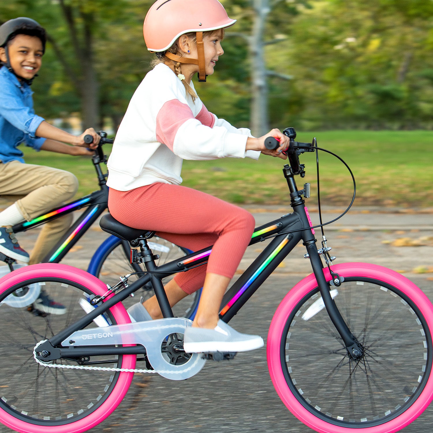 two kids riding the JLR X through the park with helmets on and smiling 