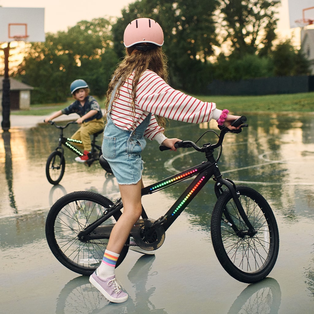 two kids riding black light up bikes on an outdoor basketball court