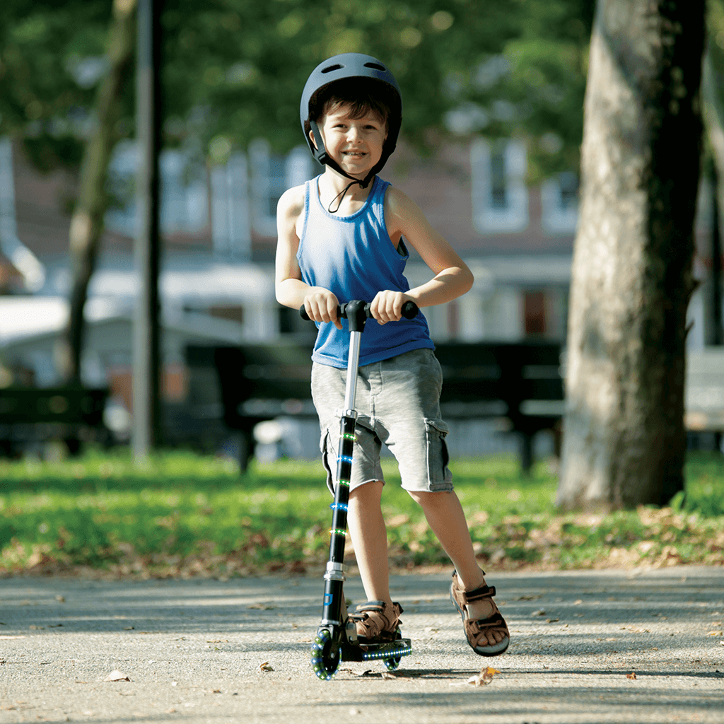 boy in a helmet riding the green and blue orbit kick scooter through the park