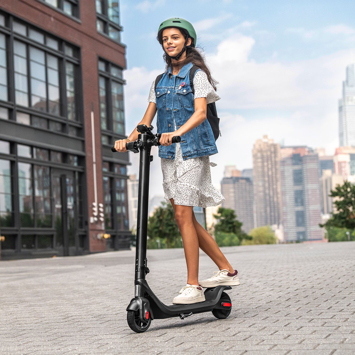 young person riding Rhythm e-scooter outside with a city landscape in the background