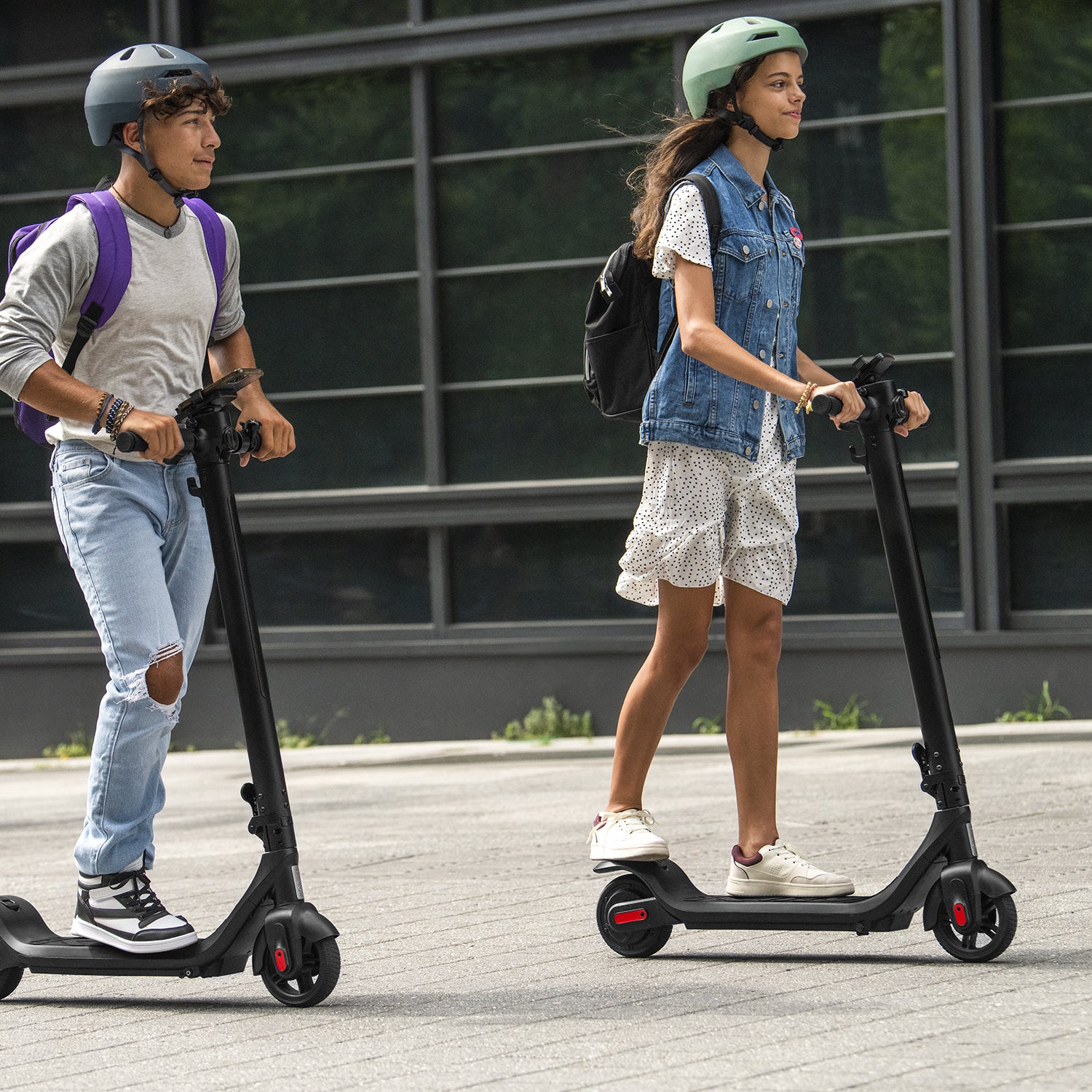 two young people riding the Rhythm e-scooter outside 