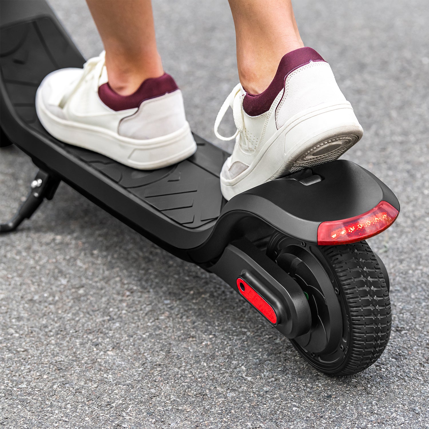 close up of the back of the Rhythm e-scooter with a person standing on it with the kickstand down