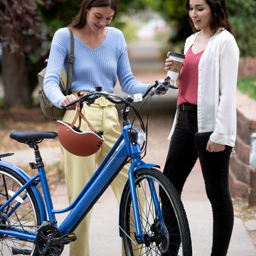 two people standing with the Journey bike and one is holding a helmet while the other is holding a cup of coffee